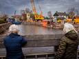 Twee dames staan op de brug belangstellend te kijken hoe het herstel van de kademuur in de kolksluis vordert.