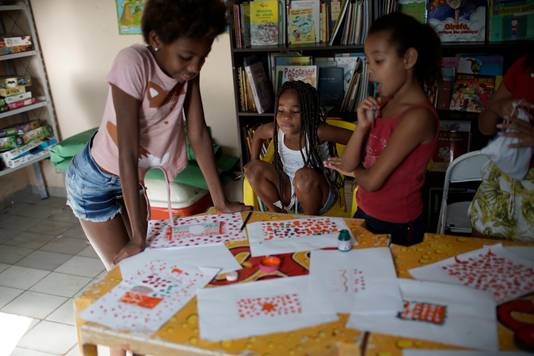 Meisjes met hun tekeningen tijdens een les in een buurtbibliotheek in de favela Morro do Salgueiro in Rio de Janeiro. Hoewel de scholen nog altijd gesloten zijn, verzorgt een lerares daar extra lessen om het gemis aan regulier onderwijs op te vangen.