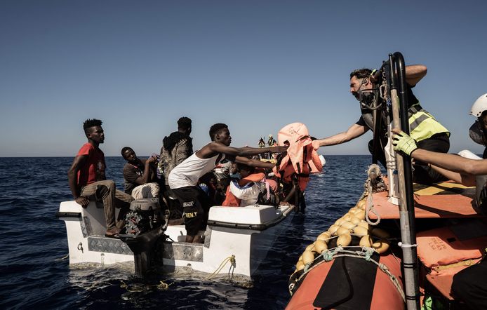 Een vrijwilliger geeft  in internationale wateren nabij Libië reddingsvesten aan een migrant, waarna de mensen aan boord van het reddingsschip worden gehaald.