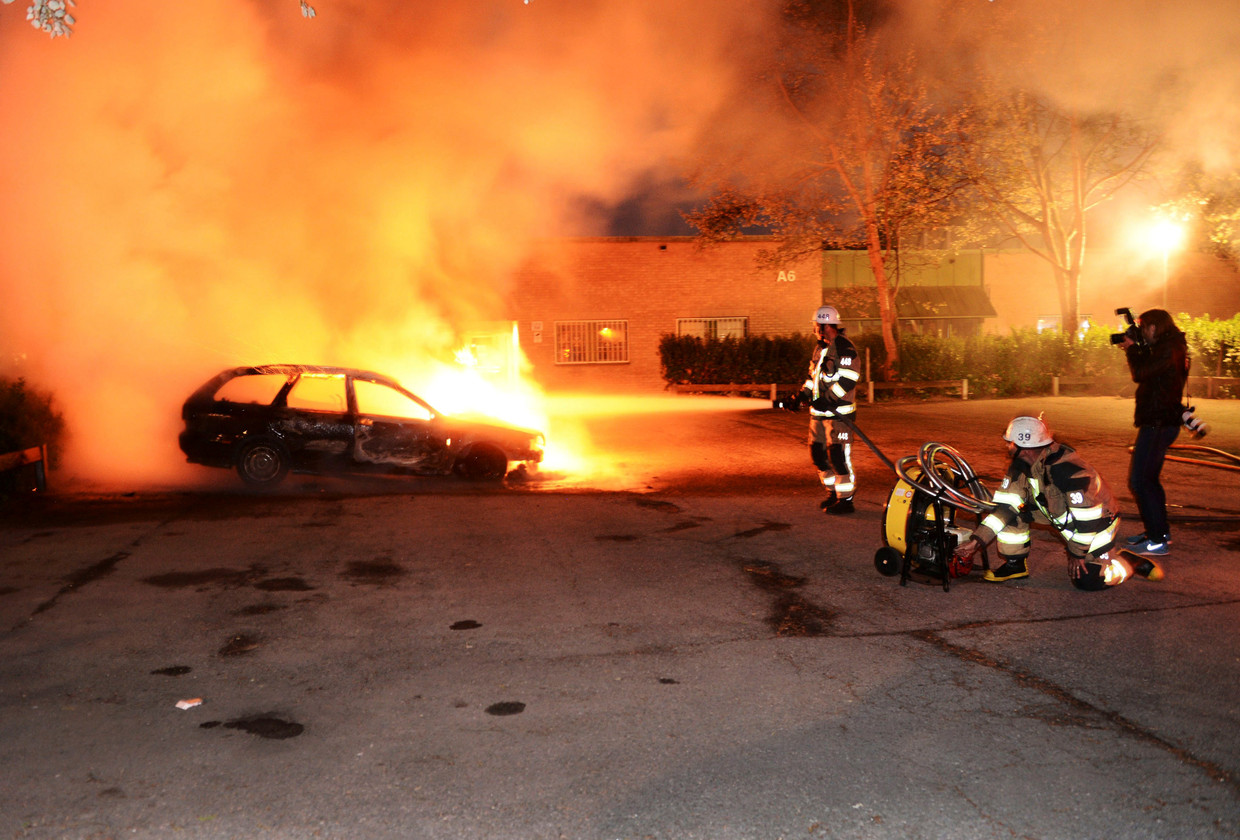 Brandweerlieden blussen een autobrand in een voorstadje van Stockholm, waar het maandagavond tot ongeregeldheden kwam. Beeld REUTERS