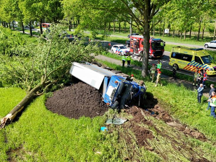 Vrachtwagen ramt boom uit de grond, kantelt en komt terecht in het gras: chauffeur naar het ziekenhuis