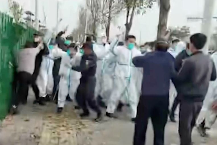 Beveiligers in witte pakken vallen de medewerkers aan van de Foxconn-fabriek in Zhengzhou, tijdens de protesten op woensdag 23 november. Beeld AP
