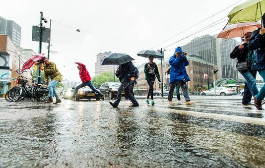 Rotterdammers banen zich een weg over de Coolsingel tijdens de regenval.