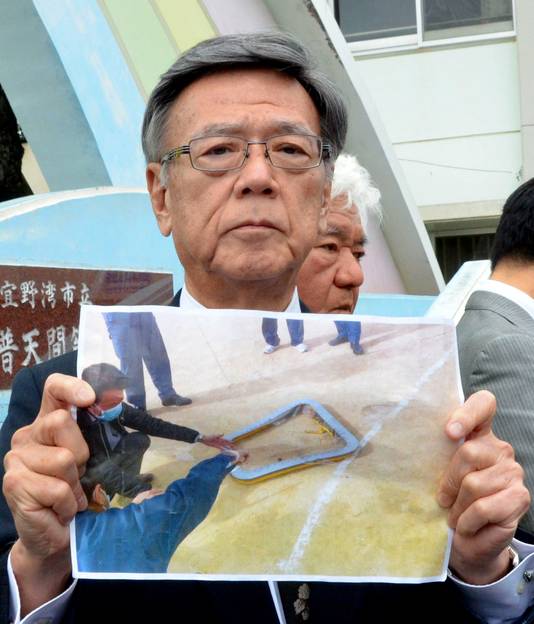Gouverneur Takeshi Onaga toont een foto van het losgeraakte helikopterraam.