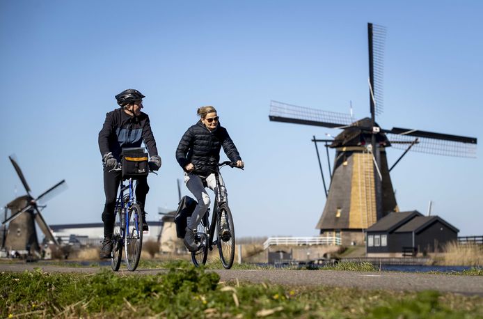 Mensen fietsen langs de molens in Kinderdijk tijdens een zonnig lenteweekend.