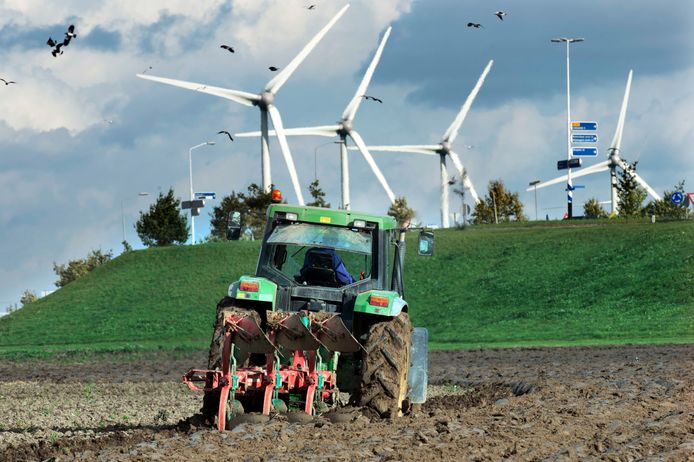 Een boer ploegt zijn akker met op de achtergrond de windmolens langs de A15 bij Echteld.