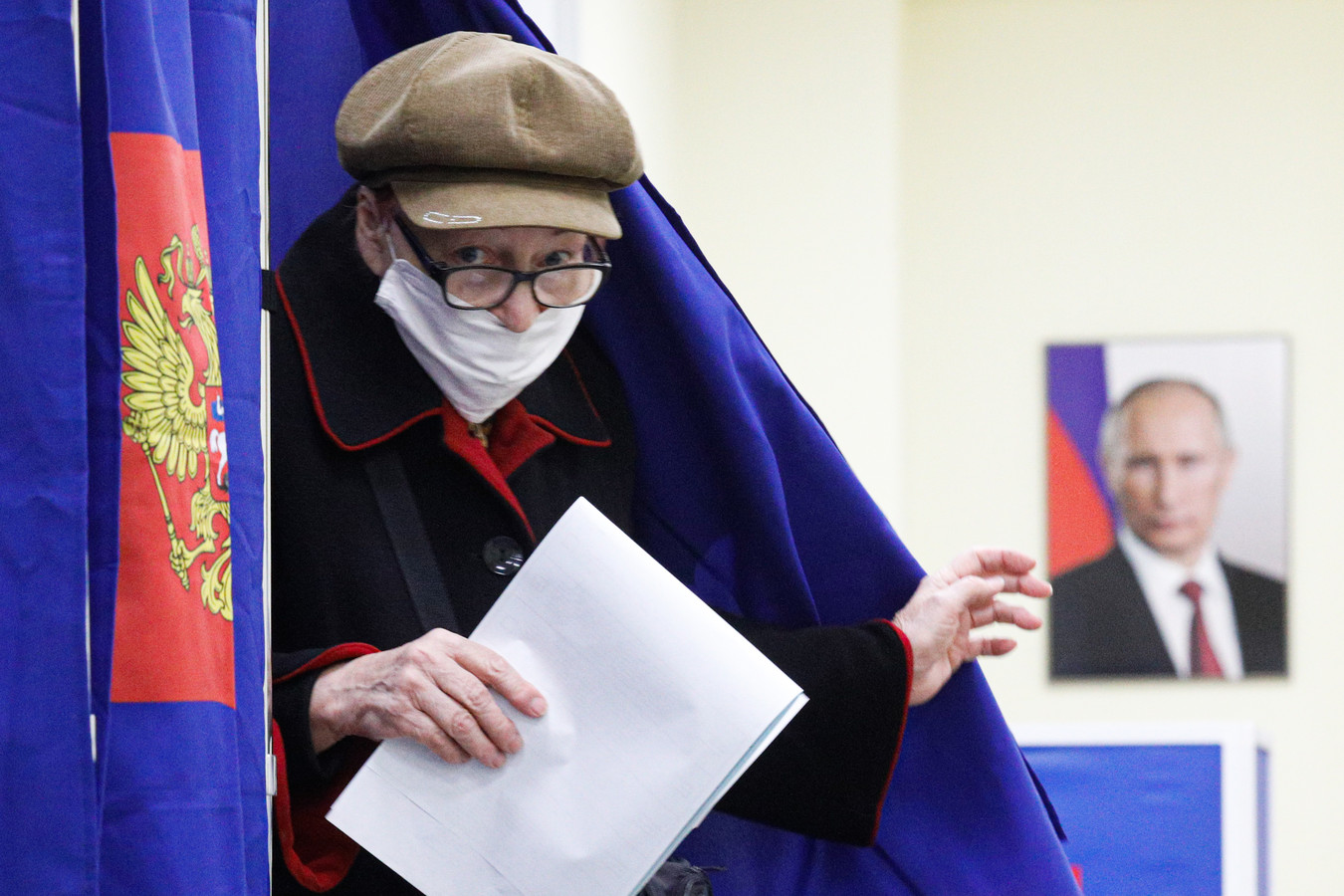 Een vrouw bij een stembureau loopt langs een portret van Poetin.