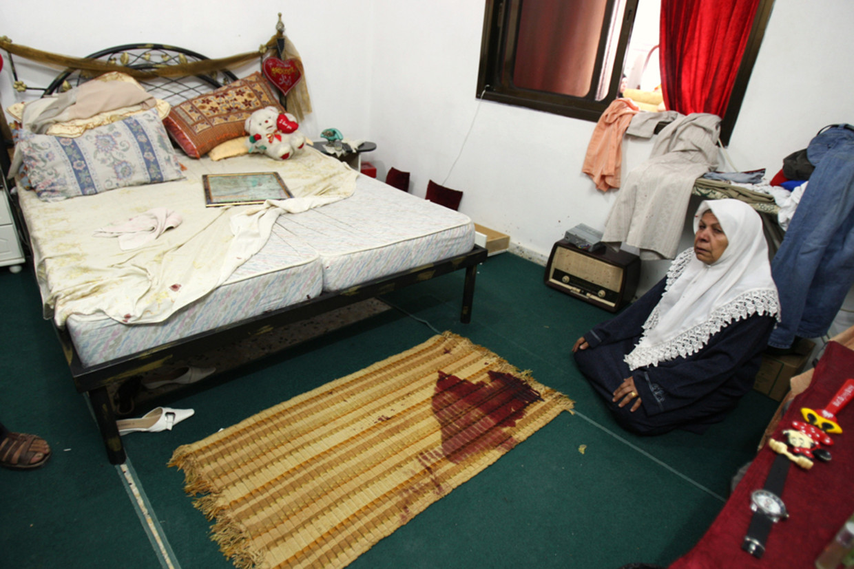 De vrouw van de vermoorde Hamas-voorman Iyad Abu Shilbaya knielt neer bij een bebloed tapijt in de slaapkamer waar hij vermoord is (AP) Beeld AP