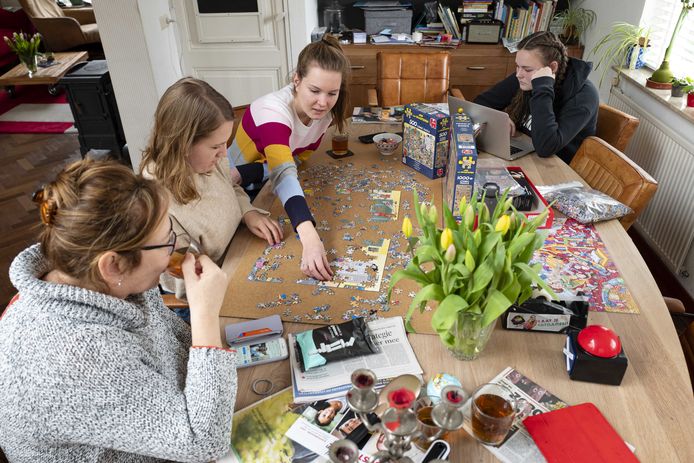 Leden van een Nederlands gezin puzzelen aan de eettafel om de tijd te verdrijven.