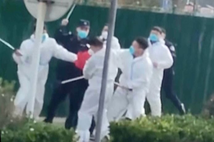 Op een foto van eind november 2022 is te zien hoe een betoger bij een fabriek van Foxconn hardhandig wordt aangepakt door bewakingsagenten.