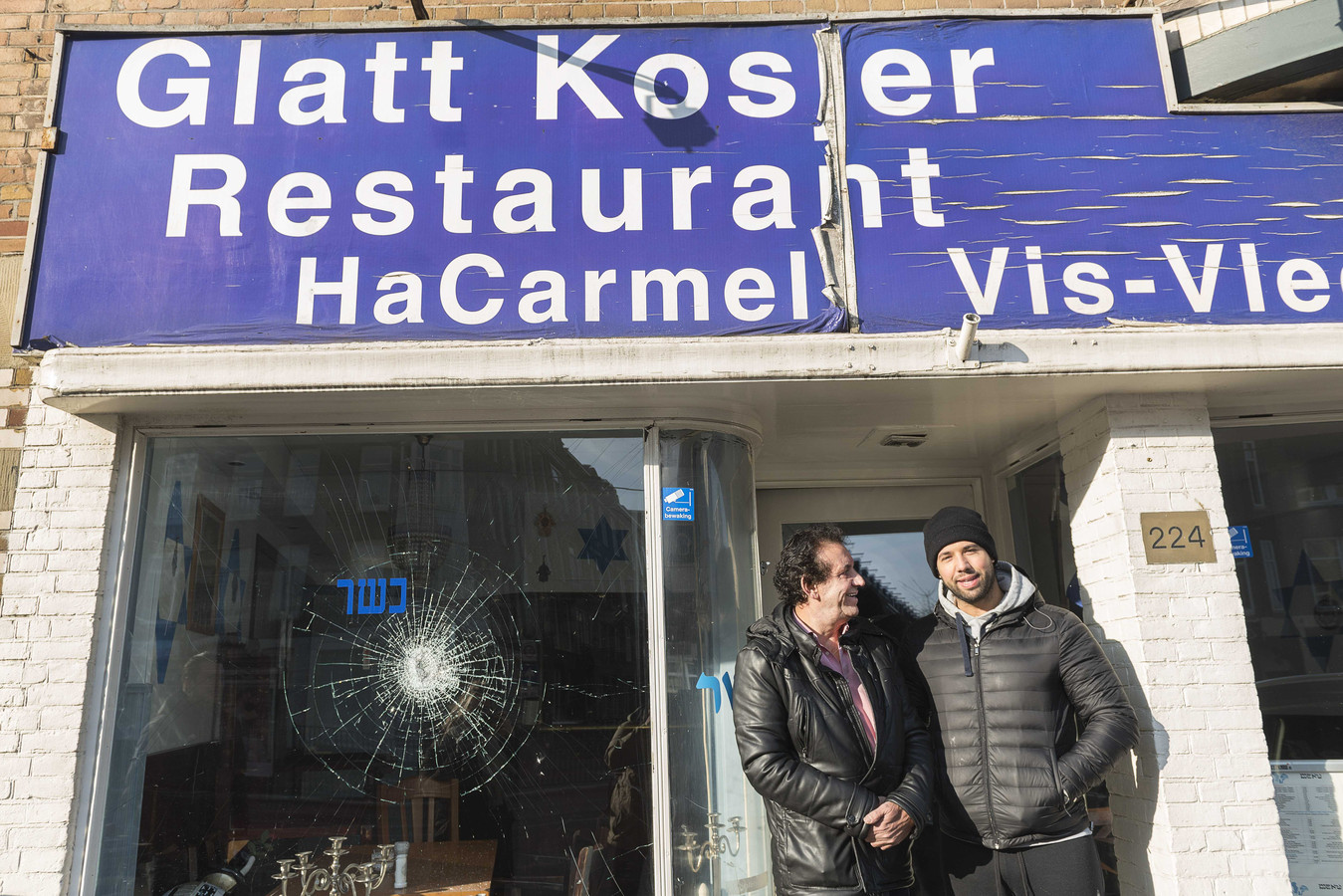 Eigenaar Daniel Baron (R) staat met zijn vader voor het Israëlische restaurant HaCarmel en laat de schade aan zijn restaurant zien.