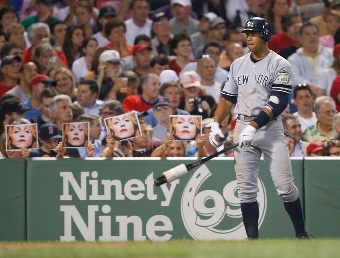 Publiek houdt foto's van Madonna omhoog terwijl honkballer Alex Rodriguez van The New York Yankees klaarstaat voor zijn slagbeurt.