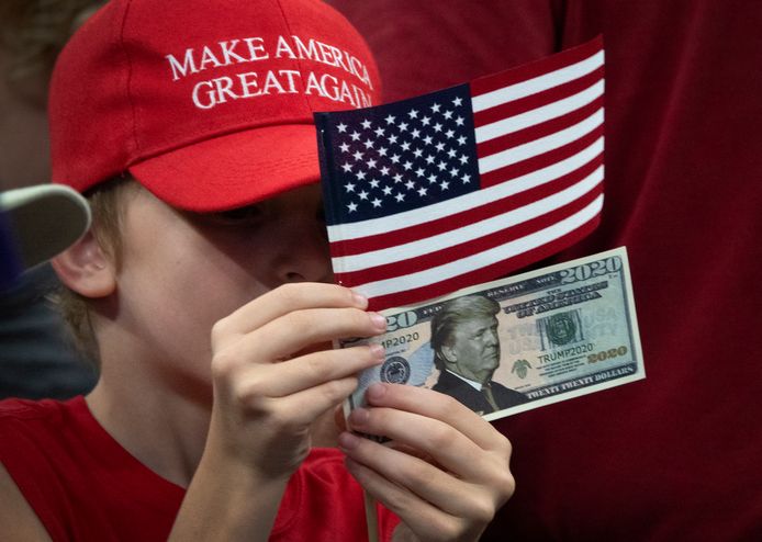 Een jeugdige Trump-aanhanger houdt een Amerikaanse vlag en een dollarbiljet met het portret van de president omhoog.