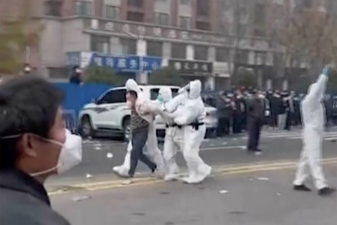 Bewakers in beschermende kleding voeren een werknemer van de Foxconn-fabriek in Zhengzhou weg (23/11/2022).