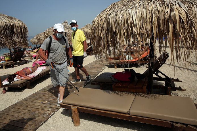 Stranden in Athene mogen terug open. Een medewerker van een beachbar desinfecteert ligbedden.