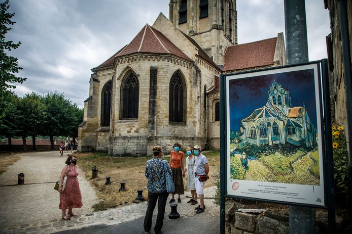 Toeristen met mondmasker luisteren naar de uitleg van de gids bij de kerk van Auvers-sur-Oise, ten noorden van Parijs. Vincent Van Gogh schilderde de kerk vlak voor zijn dood in 1890.