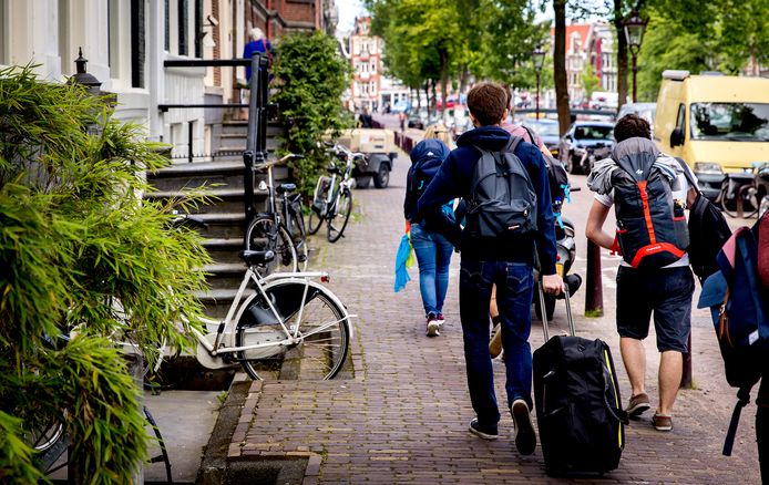 Toeristen met rolkoffers op de grachten in Amsterdam.