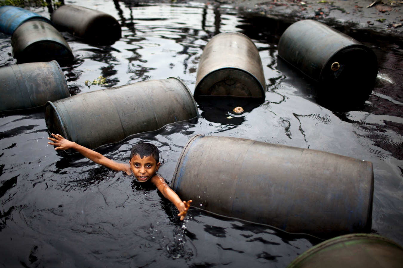Een jongen zwemt in een vergiftigde rivier vol met olievaten in Dhaka, Bangladesh.