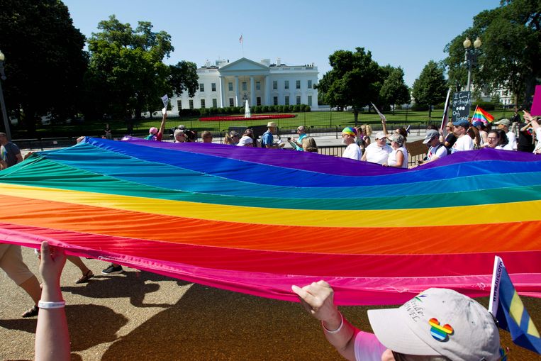 Amerikanen lopen met een grote regenboogvlag voorbij het Witte Huis in Washington. Archiefbeeld. Beeld AFP
