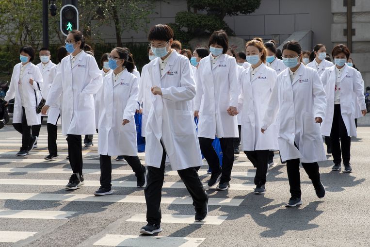 Artsen uit Peking wandelen over straat in Wuhan, waar de lockdown langzaam wordt opgeheven.  Beeld AP