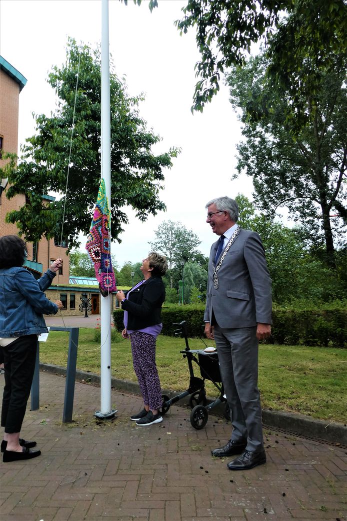 De gebreide vlag gaat in top. Loco-burgemeester Ed Mathijssen kijkt toe.