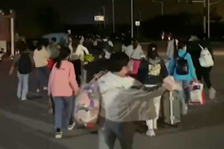 Mensen met koffers en zakken verlaten de Foxconn-fabriek in Zhengzhou. Beeld AP