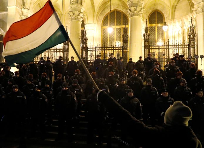 Politieagenten vormen een cordon voor het parlementsgebouw in de Hongaarse hoofdstad Boedapest terwijl demonstranten betogen tegen de nieuwe arbeidswet.