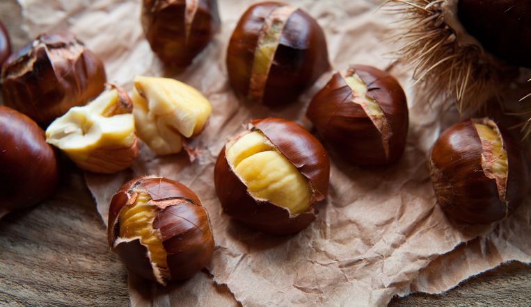 Traditional Christmas dish  - Ripe Sweet Roasted Chestnuts, cracked shells after put to the fire, natural paper and old wooden rustic background. Beeld Getty Images/iStockphoto