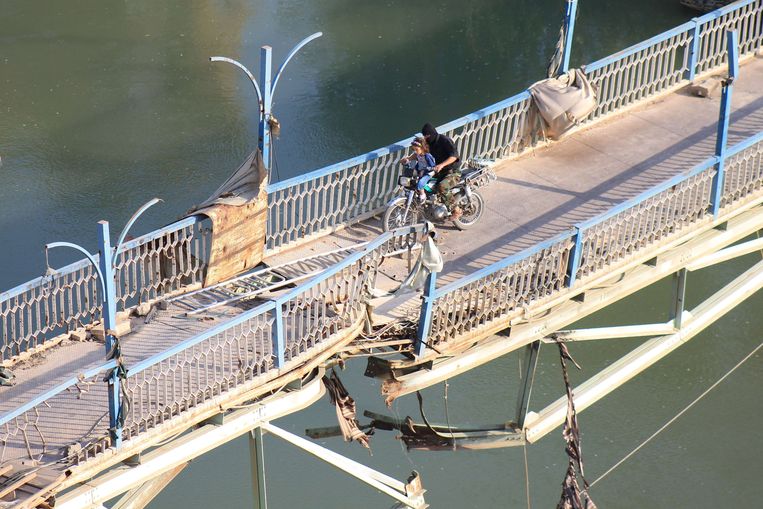 Een Syrische oppositiestrijder en een kind op een fiets over een beschadigde brug in Deir Ezzor, vandaag. Beeld AFP