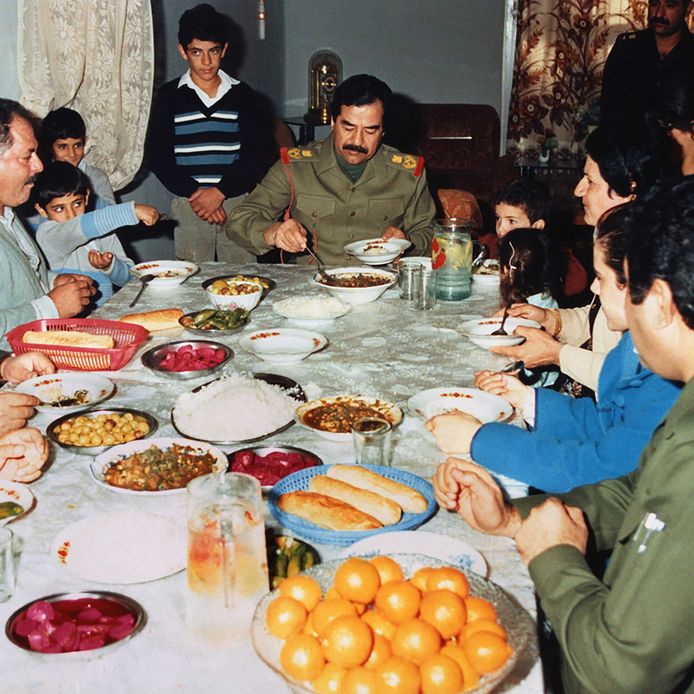 Saddam Hoessein prikt een vorkje mee bij een familie in Basra. Het is 1986, Irak is in oorlog met Iran.