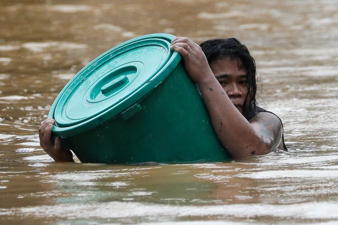 Een vrouw gebruikt een plastic vuilnisbak als reddingsboei bij een grote overstroming in Marikina op de Filipijnen als gevolg van de tyfoon Vamco.