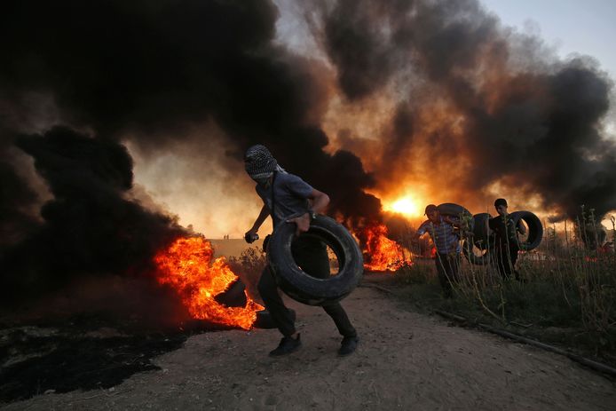 Palestijnse betogers dragen autobanden naar een al brandende stapel tijdens een confrontatie met het Israëlische leger in de Gazastrook.