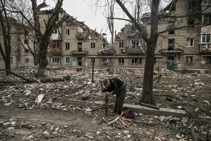 Een oudere man sprokkelt hout voor een verwoest appartementsgebouw in de stad Avdiivka.