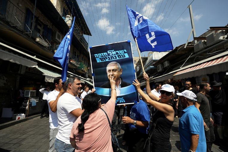 Supporters van Benjamin Netanyahu houden een verkiezingsposter van de langstzittende premier omhoog op de markt van Jeruzalem.  Beeld Ammar Awad / Reuters