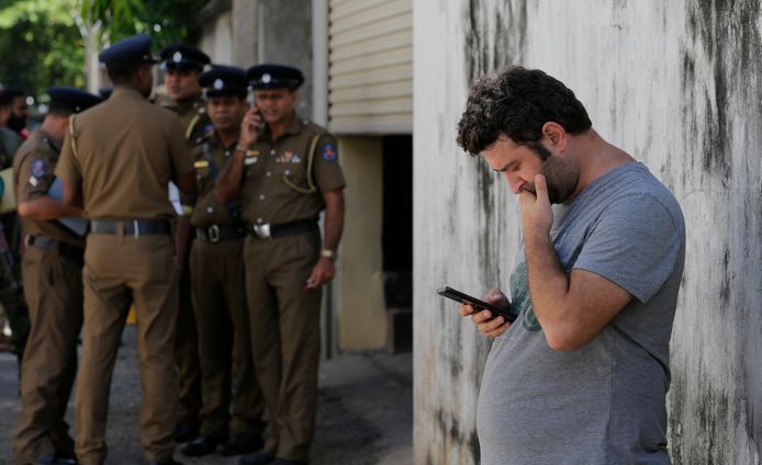 Een toerist in Sri Lanka kijkt, voor het mortuarium van een ziekenhuis, op zijn telefoon.