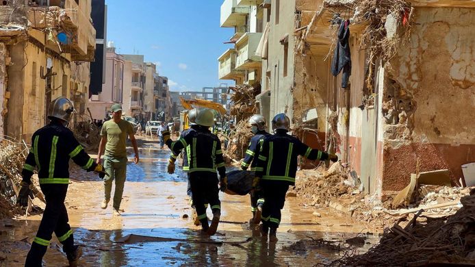 Reddingsteams dragen een lichaam weg terwijl ze door de modder en tussen vernielde gebouwen stappen in Derna.