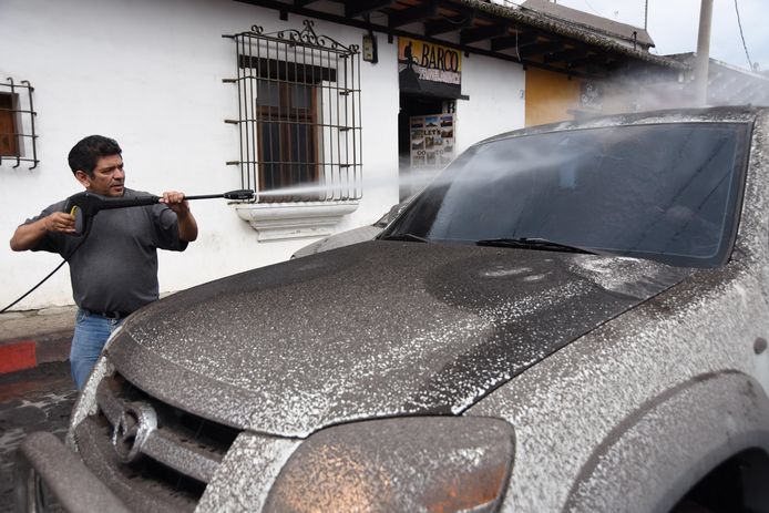 Een man maakt zijn auto schoon, die helemaal onder de as zit van de uitbarstende vulkaan.