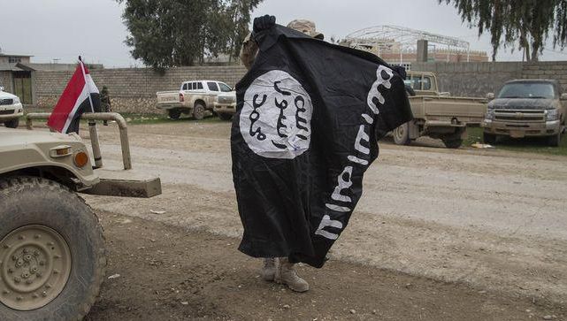 Een lid van het Iraakse leger neemt een vlag van IS in beslag in Mosoel.