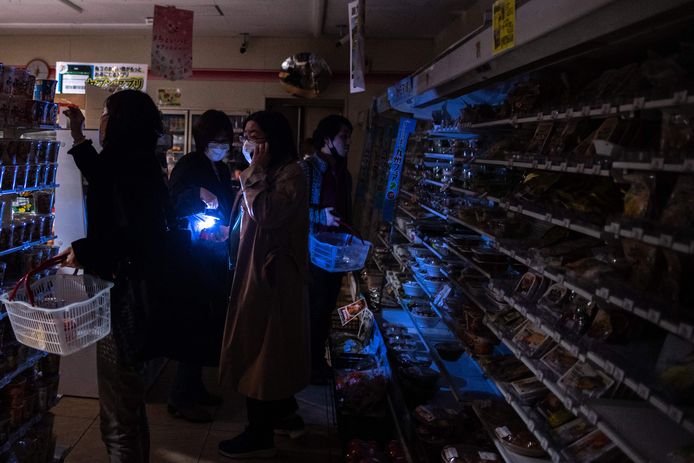 In grote delen van Tokio is de stroom uitgevallen. Klanten van een supermarkt doen in het donker boodschappen.
