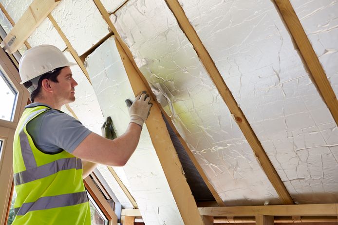 Een bouwvakker brengt dakisolatie aan in een woning. Goede isolatie kan zorgen voor minder CO2-uitstoot.