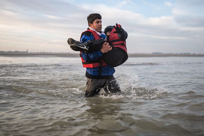 Een migrant draagt een kind terwijl hij in Frankrijk naar een smokkelaarsboot rent om het Kanaal mee over te steken.