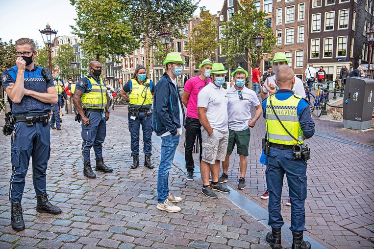 Zondagavond op de Wallen: handhavers hebben zojuist een aantal Duitse toeristen aangesproken omdat ze geen mondkapje droegen. Nu dus wel. Beeld Guus Dubbelman / de Volkskrant