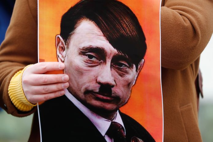 Betogers bij de Russische ambassade in Riga, Letland, houden een afbeelding van Poetin als Adolf Hitler op.