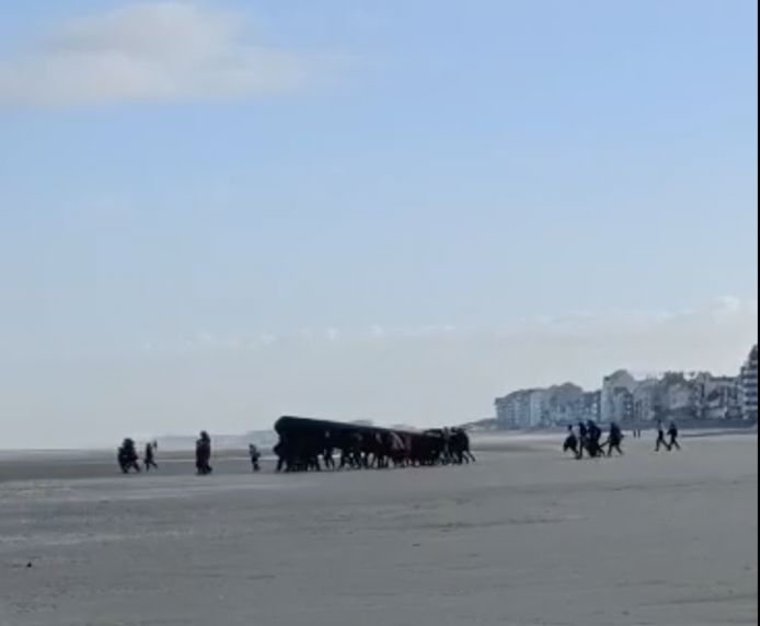 De transmigranten lopen met de grote boot over het strand.