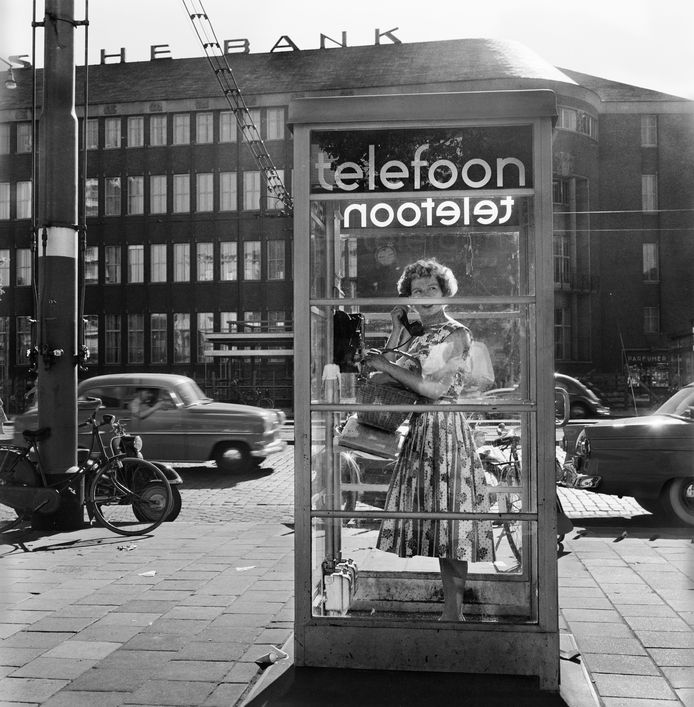Een vrouw belt in een telefoon­cel op het Beursplein, circa 1957-1960. Met op de achtergrond een gedeelte van het Rotterdamsche Bankgebouw aan de Coolsingel.