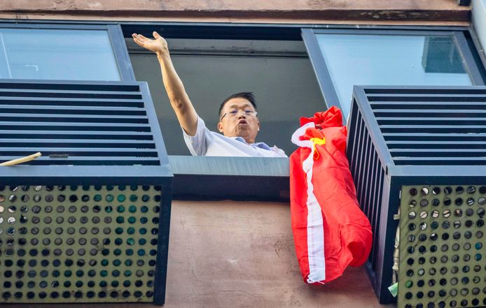 Een man zwaait vanuit een raam aan de overkant met een Chinese vlag naar het Amerikaanse consulaat in Chengu.