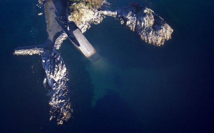 De betonnen constructie komt als een walvis met zijn bek open onopvallend tussen twee rotspunten te liggen.