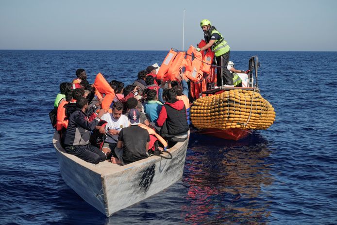 Bemanningsleden geven reddingsvesten aan migranten in een houten bootje op zee.