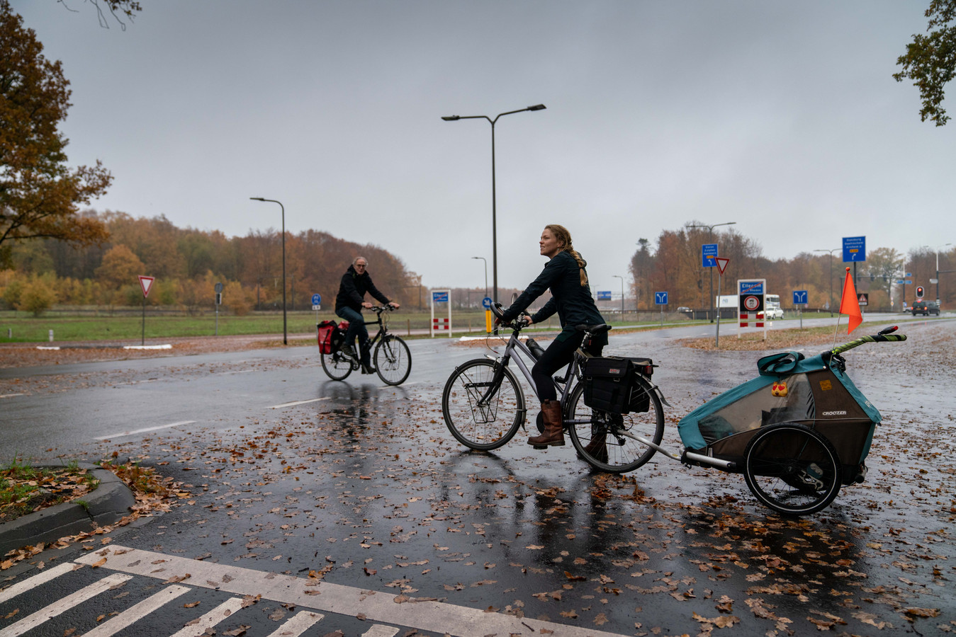Hiske Feenstra (rechts, met achter zich haar zoon Kris, steekt bij Ellecom de Zutphensestraatweg over om bij de verderop gelegen fietstunnel te kunnen komen. Links Freek te Brinke.