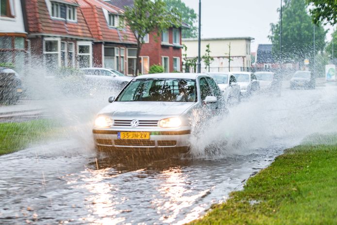 Een auto rijdt door een ondergelopen straat in Sappemeer nadat een hevige regenbui overgetrokken is.